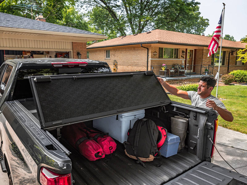 UnderCover Select held part-open mid-fold with the bed loaded with coolers, backpacks and bags on a driveway.