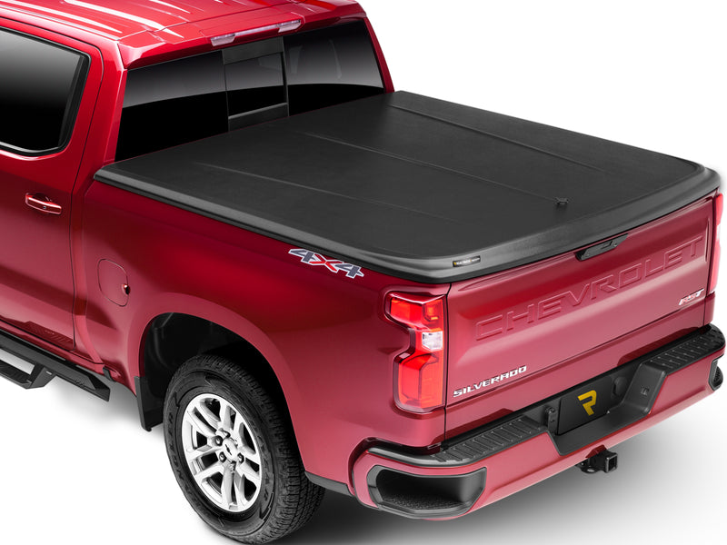 UnderCover SE one-piece tonneau cover closed and latched on a pickup bed, rear three-quarter studio view, the black textured lid sitting flush across the tailgate with no bed floor showing.