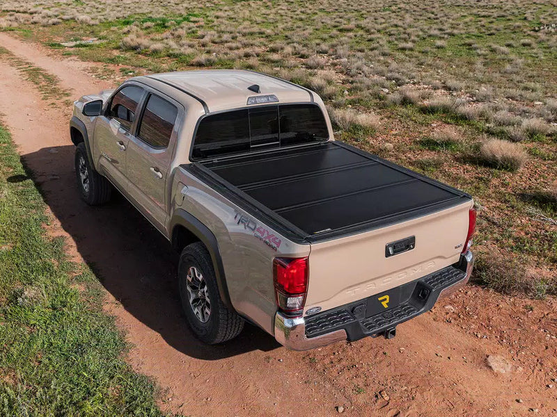 UnderCover Ultra Flex hard folding tonneau cover closed and flush on a pickup parked on a grassland track, rear three-quarter view.