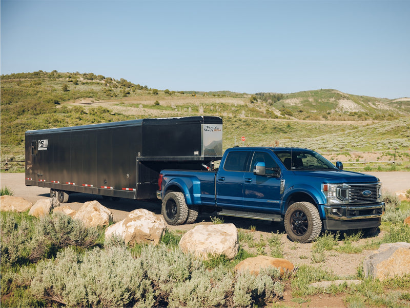 ReadyLIFT 10-Lug Dual Steering Stabilizer Kit installed on a blue Ford F-450 Super Duty dually towing a gooseneck trailer