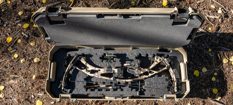 Desert Tan DECKED Honcho 80 open on the ground with a compound bow and arrows seated in the cut-out PuzzleFoam
