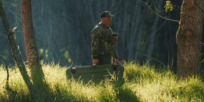 Hunter carrying a closed Ranger Green DECKED Honcho 80 through tall grass at first light