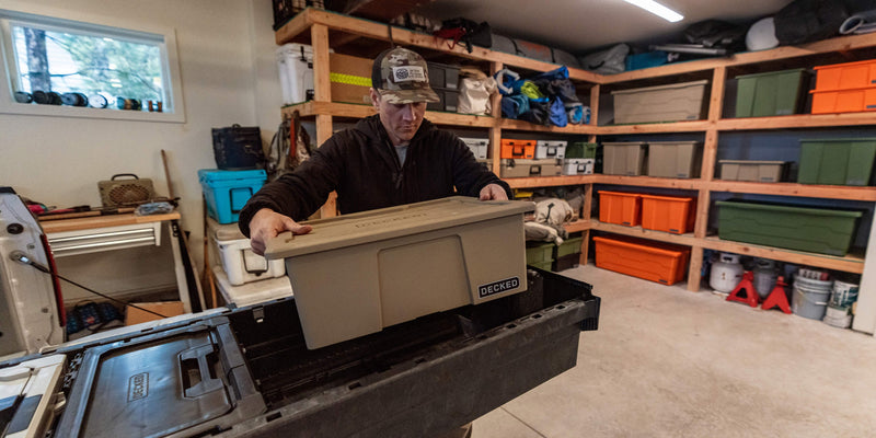 Owner lowering a Desert Tan DECKED Payloader 32 into a DECKED Drawer System drawer in a gear-lined garage
