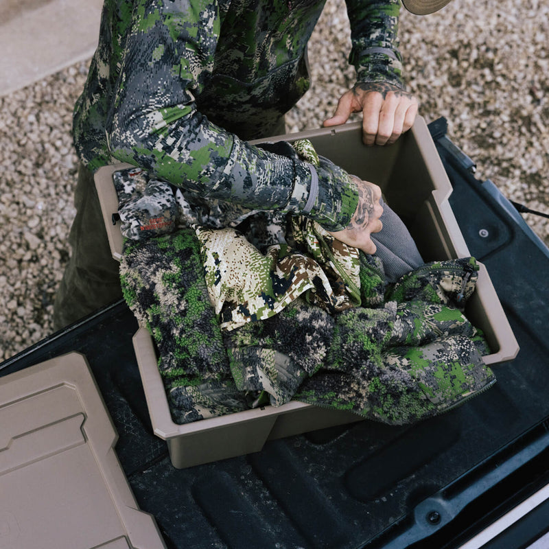 Hunter packing camouflage clothing into a Desert Tan DECKED Payloader 32 on a tailgate