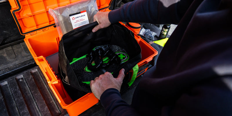 Hands packing the recovery strap bag into the Blaze Orange DECKED Roadside Emergency OS Kit case on a tailgate