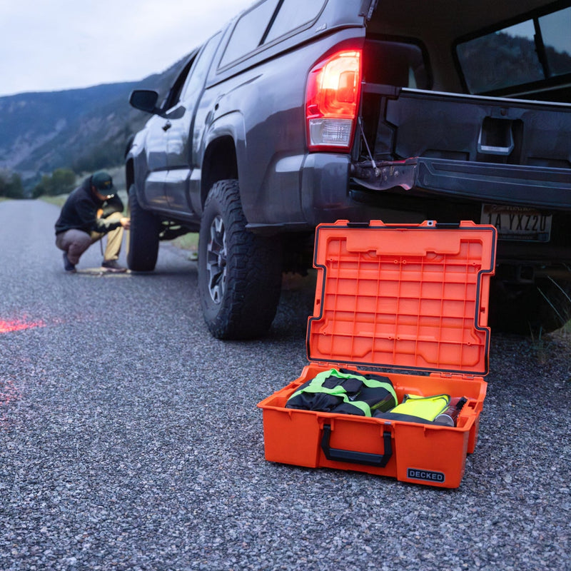 The open Blaze Orange DECKED Roadside Emergency OS Kit on the shoulder while a driver changes a tire at dusk