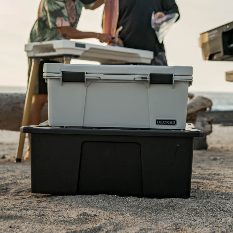 Cool Gray DECKED Sixer 16 stacked on a larger black DECKED case on a beach