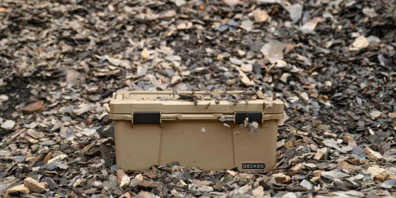 Desert Tan DECKED Sixer 16 sitting closed on dark shale rock outdoors