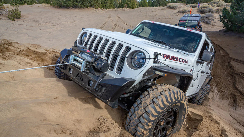 White Jeep Wrangler Rubicon winching itself along a sand bank with a Warn ZEON XC mounted in the front bumper