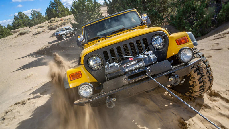 Yellow Jeep Wrangler winching itself up a sand dune with a Warn ZEON XC mounted in the front bumper