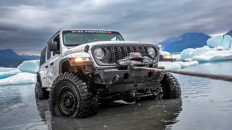 Warn ZEON XP winch pulling line from a white Jeep Wrangler standing in glacial melt water among ice floes