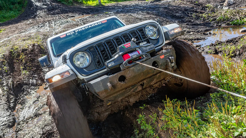 Warn ZEON XP winch pulling a Jeep Wrangler out of a deep mud rut, line running out to an anchor