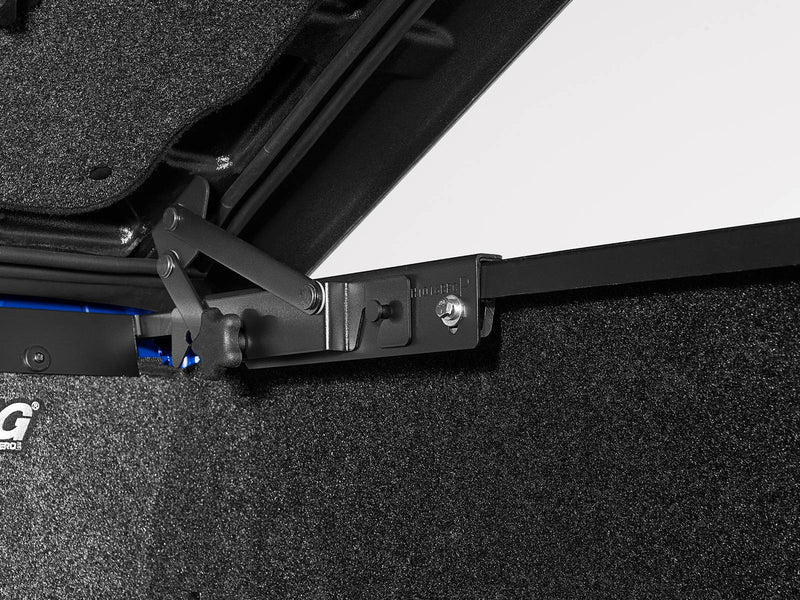 Close-up of the hinge and prop arm at the forward edge of the lid where it meets the bed rail.