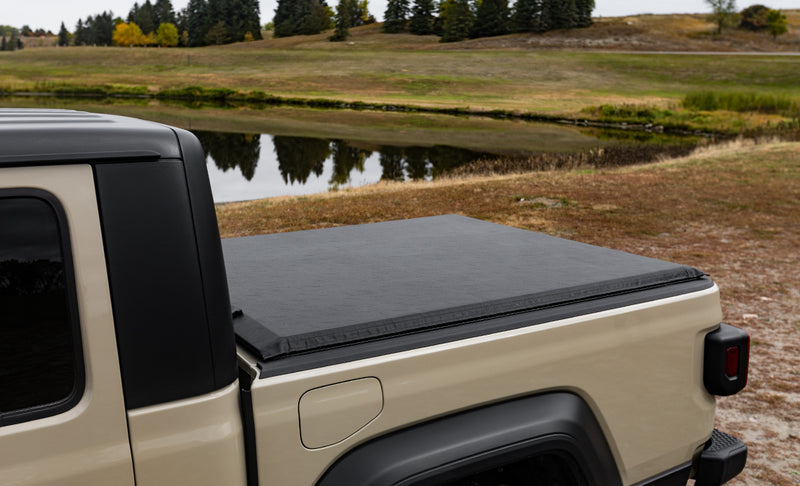 Access Limited Edition roll-up tonneau cover on a pickup bed: black vinyl roll-up cover closed over a tan pickup bed beside a pond