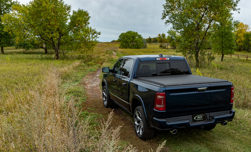 Access Limited Edition roll-up tonneau cover on a pickup bed: dark blue crew cab pickup on a grassy two-track with a black roll-up cover closed over the bed