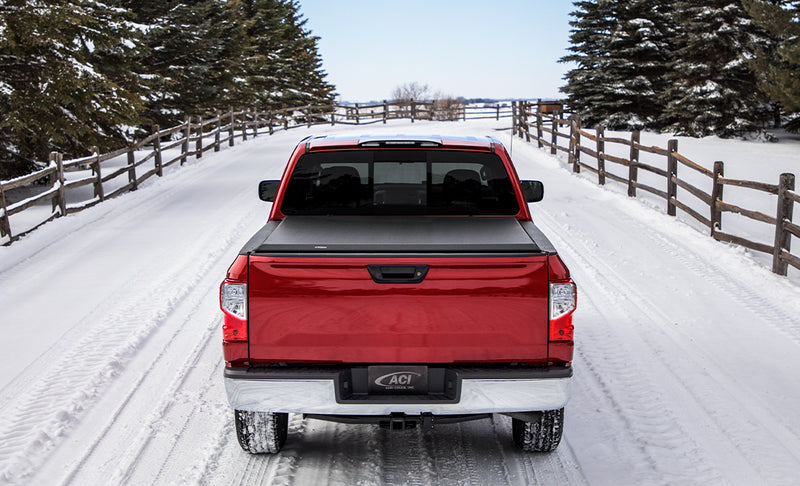 Access Limited Edition roll-up tonneau cover on a pickup bed: red pickup on a snowy lane, rear view, black roll-up cover closed flat over the bed