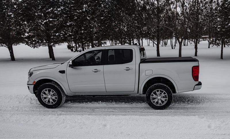 Access Limited Edition roll-up tonneau cover on a pickup bed: silver crew cab pickup in snow, side profile, with a low black roll-up cover closed over the bed