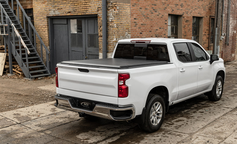 Access Limited Edition roll-up tonneau cover on a pickup bed: white crew cab pickup by a brick building with a black roll-up cover closed over the bed