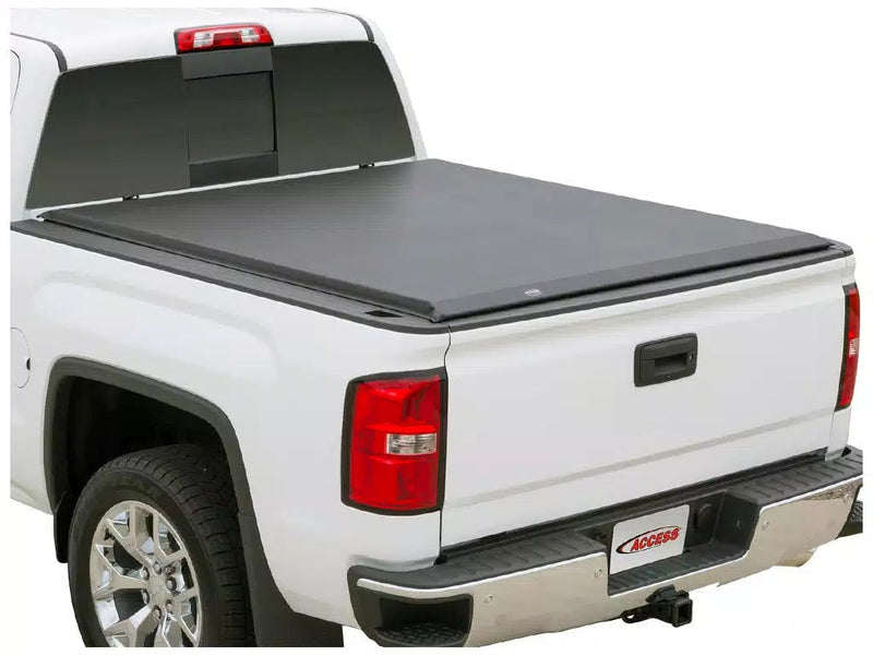 Full view of the Access Limited Edition roll-up tonneau cover: white pickup on white with a black vinyl roll-up cover closed flat over the bed, rear three-quarter (trailer hitch receiver shown, not included)