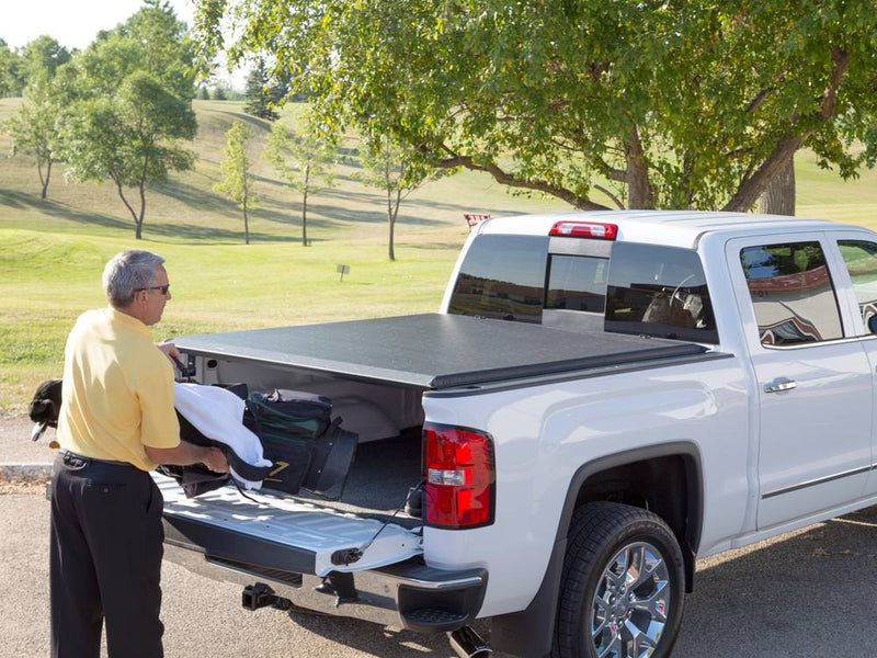 Man loading a golf bag through the open tailgate under the closed roll-up cover