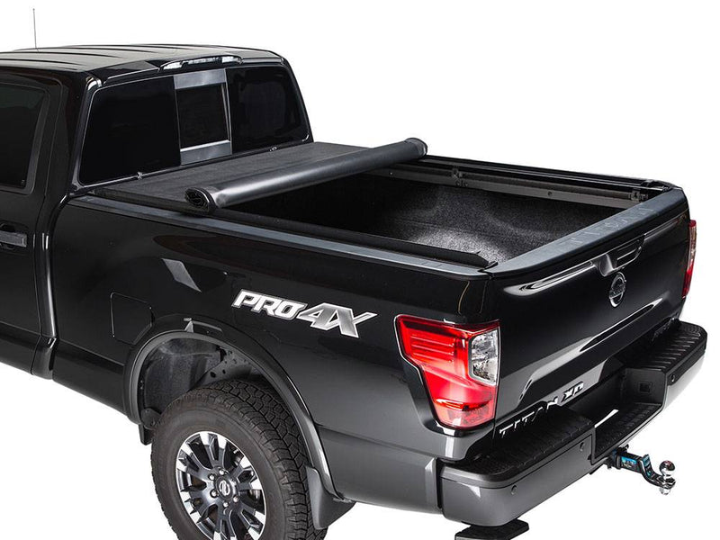 Black pickup with the roll-up cover rolled halfway toward the cab, carpeted bed exposed, white background