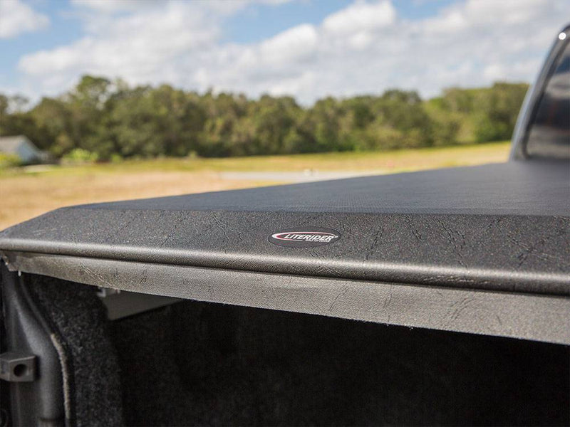 Rear edge of the closed black vinyl cover with its small brand badge, tailgate open