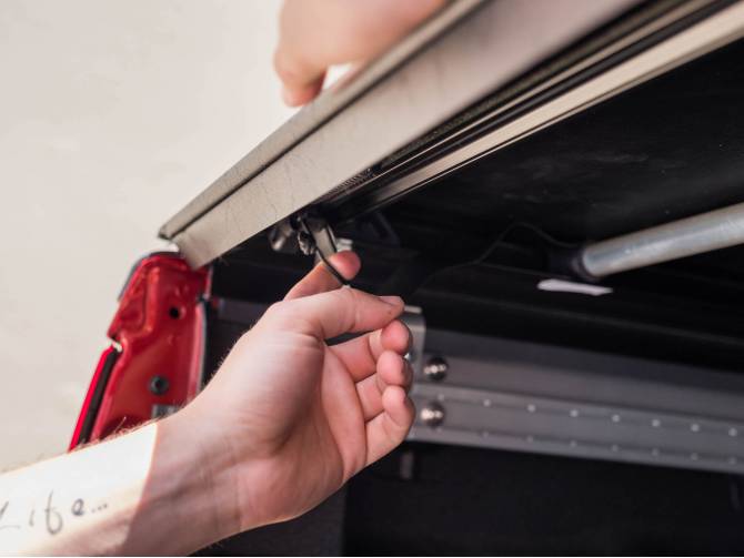 Hand pulling the rear latch release under the edge of the vinyl cover at the tailgate