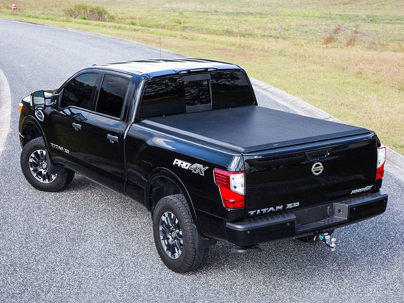 Black crew cab pickup on a curving road with a black roll-up tonneau cover closed over the bed