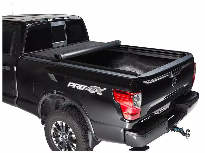 Full view of the Access LiteRider roll-up tonneau cover: black pickup with the roll-up cover rolled halfway toward the cab, carpeted bed exposed, white background (trailer hitch ball mount and bed mat shown, not included)