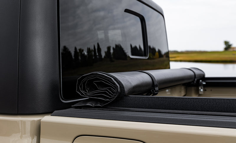 Close-up of the Access LiteRider roll-up tonneau cover: close-up of a black vinyl cover rolled up and strapped against the cab of a tan pickup