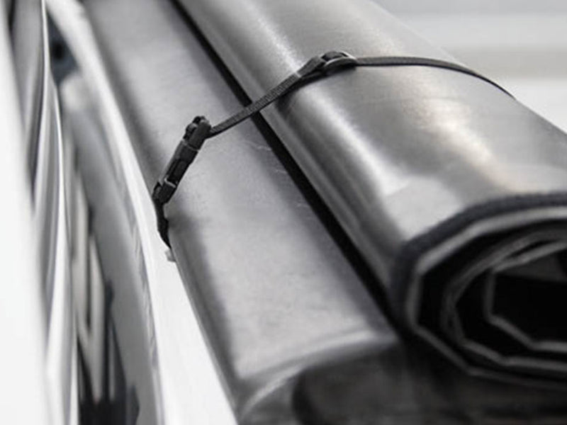 Close-up of the Access LiteRider roll-up tonneau cover: close-up of a rolled black vinyl cover wrapped with a thin storage strap and buckle