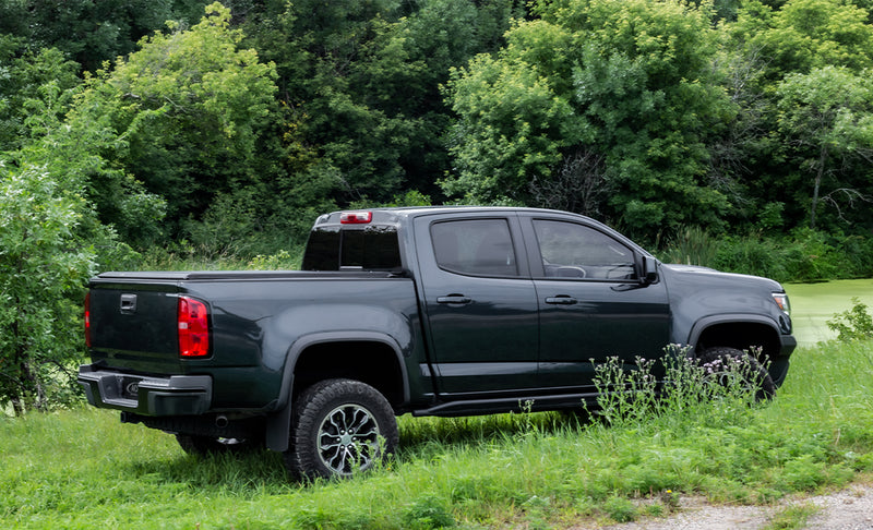 Access LiteRider roll-up tonneau cover on a pickup bed: dark green crew-cab pickup parked in tall grass with a black roll-up cover closed over the bed