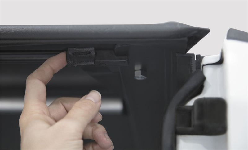 Close-up of the Access LiteRider roll-up tonneau cover: hand pulling the latch release under the rear edge of a black vinyl roll-up cover