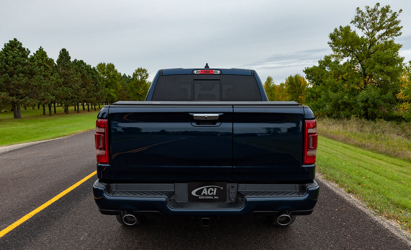Access LiteRider roll-up tonneau cover on a pickup bed: rear view of a dark blue pickup on a country road with a black roll-up cover closed over the bed
