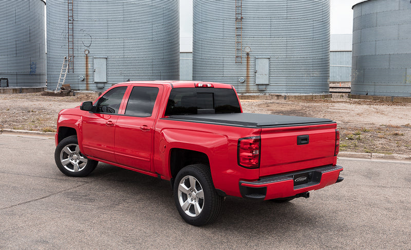 Access LiteRider roll-up tonneau cover on a pickup bed: red crew-cab pickup in front of grain bins with a black roll-up cover closed over the bed