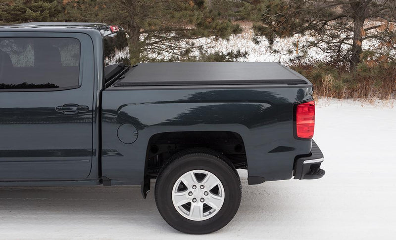 Access LiteRider roll-up tonneau cover on a pickup bed: side view of a dark green pickup on snow with a black roll-up cover closed over the bed