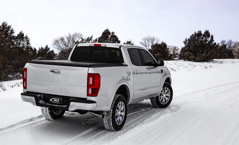 Access LiteRider roll-up tonneau cover on a pickup bed: silver crew-cab pickup on a snowy road with a black roll-up cover closed over the bed