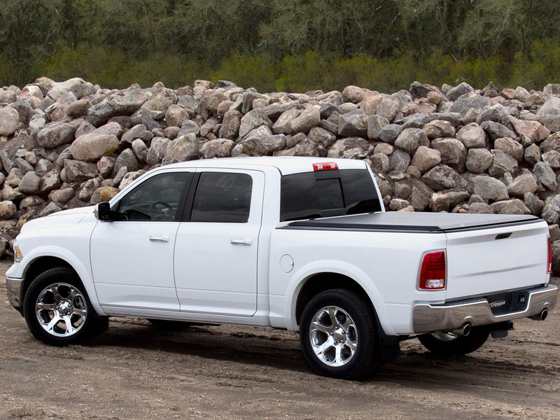 Access LiteRider roll-up tonneau cover on a pickup bed: white crew cab pickup with a black roll-up cover closed flat over the bed, parked before a rock pile