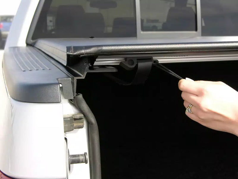 Hand pulling a cord to release the rear of the vinyl cover, tailgate down on a white pickup