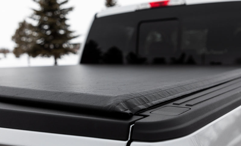 Close-up of the Access Lorado roll-up tonneau cover: close-up of a black vinyl roll-up cover's rear corner resting on a low side rail over a white pickup bed