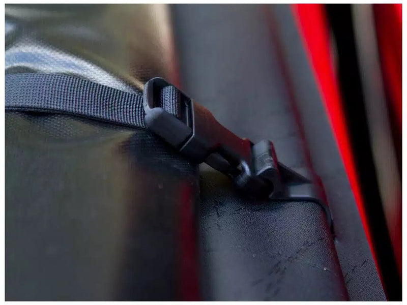 Close-up of the Access Lorado roll-up tonneau cover: close-up of a nylon storage strap and black plastic buckle on the vinyl tarp edge
