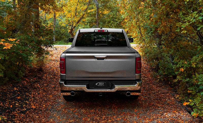 Access Lorado roll-up tonneau cover on a pickup bed: gray pickup on a leaf-covered lane, rear view, with a low black roll-up cover closed over the bed (trailer hitch receiver shown, not included)