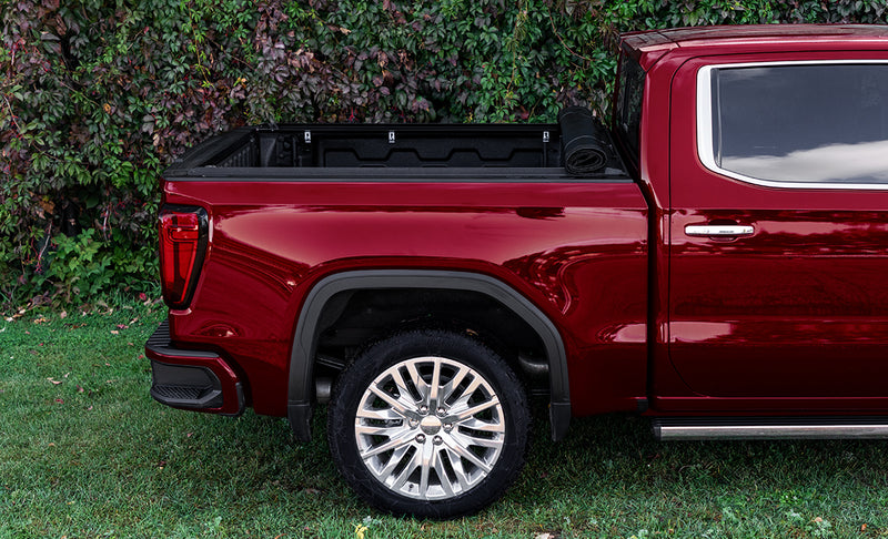 Access Lorado roll-up tonneau cover on a pickup bed: red crew cab pickup in side view with the roll-up cover rolled tight against the cab (running boards shown, not included)