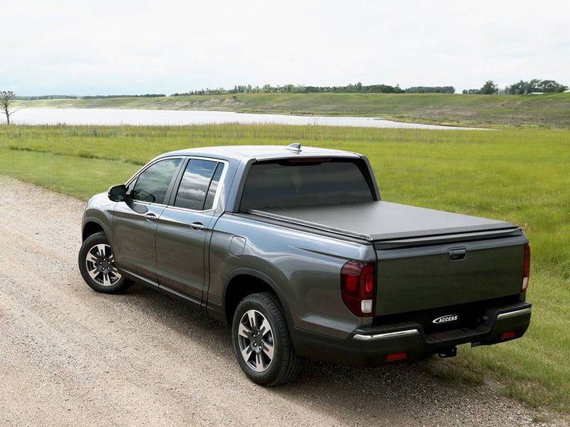Low-profile black roll-up cover closed over the bed, rear view on a gravel road by a lake
