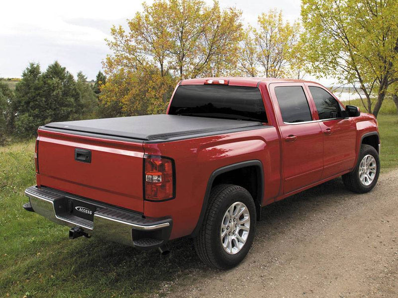 Black roll-up tonneau cover closed over the bed of a red pickup on a dirt track, Access logo plate
