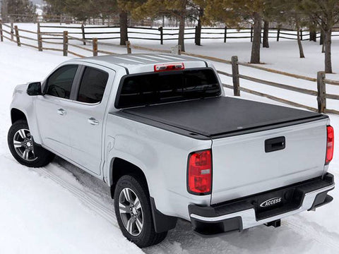 Black roll-up tonneau cover closed taut over the bed, rear three-quarter view on a snowy lane