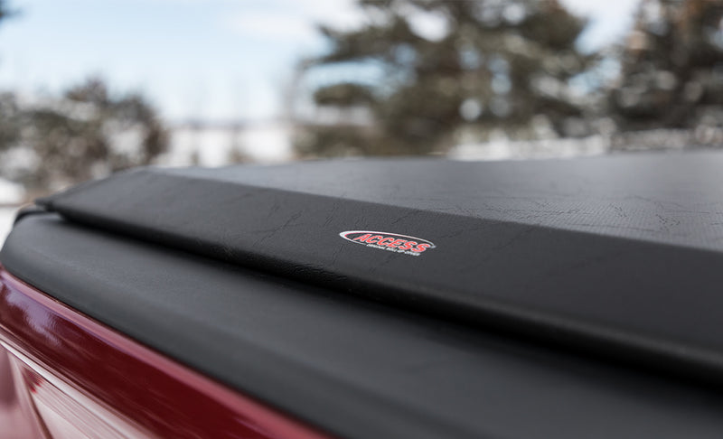 Close-up of the Access Original roll-up tonneau cover: close-up of a black vinyl roll-up cover's rear edge with a red ACCESS logo patch