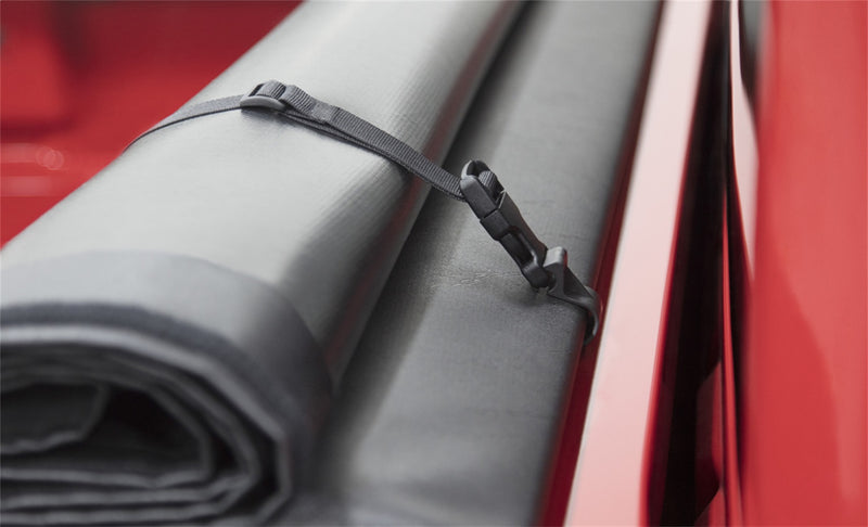 Close-up of the Access Original roll-up tonneau cover: close-up of a rolled vinyl cover secured by a nylon storage strap and buckle on a red pickup
