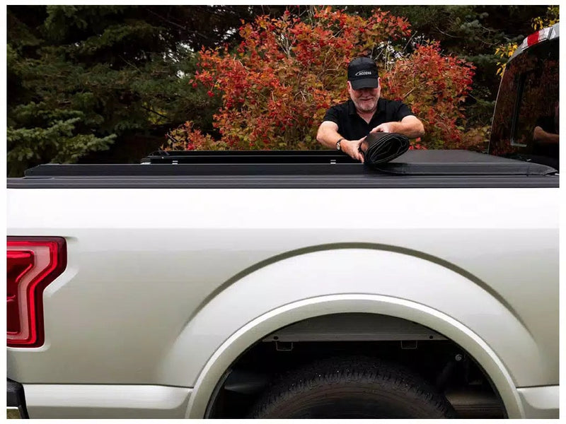 Access Original roll-up tonneau cover on a pickup bed: man in a cap rolling a vinyl tonneau cover up from the tailgate end on a silver pickup