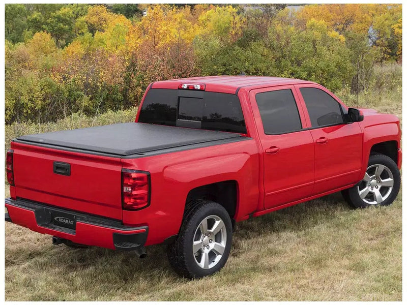 Access Original roll-up tonneau cover on a pickup bed: red crew cab pickup in autumn grass with a black roll-up cover closed flat over the bed